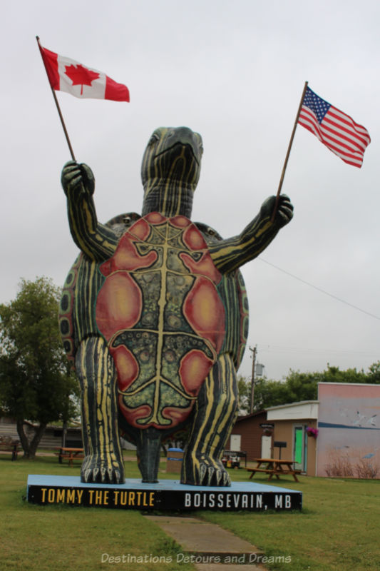 Roadside attraction of giant turtle sculpture standing on hind legs and wave Canadian and American flags