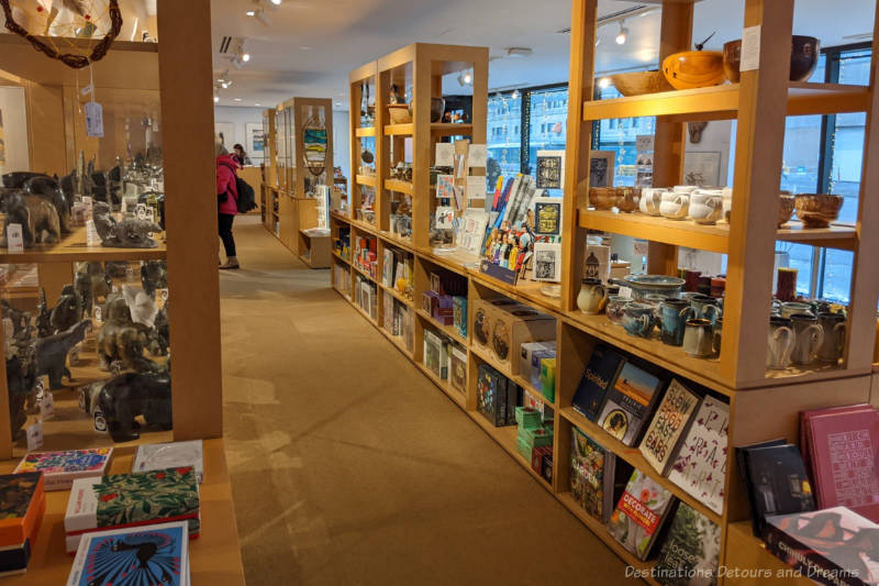 An aisle in a shop with light-coloured wood shelving containing a variety of art and home decor items