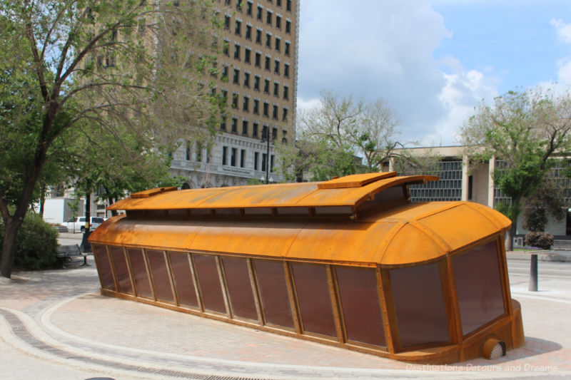 Winnipeg Bloody Saturday Sculpture Public art sculpture of an full-size orangish street car leaning at a tilt in a cement footing