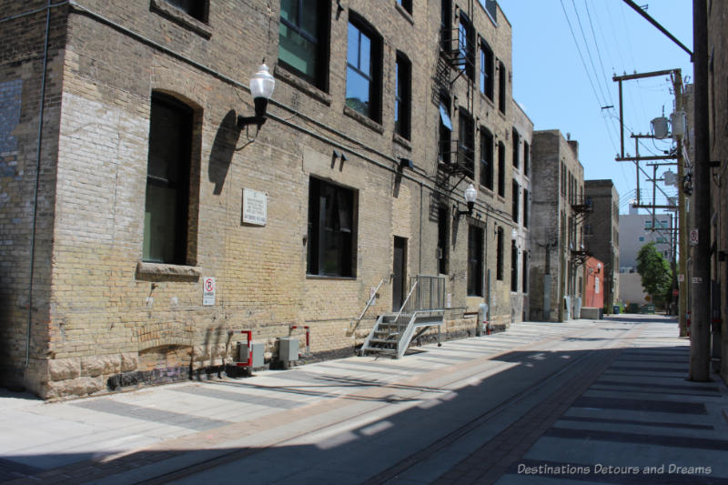 Winnipeg Hell's Alley Alley-sized street running between old brick warehouses with remnants of old spur rail lines still in street