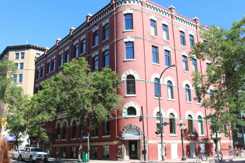 Winnipeg Stovel Block Five storey early 20th-century Romanesque Revival-style pinkish-red brick designed to fit onto corner lot with rounded corned featuring arched decorations over lower level windows and green looped decorative banner just below roofline