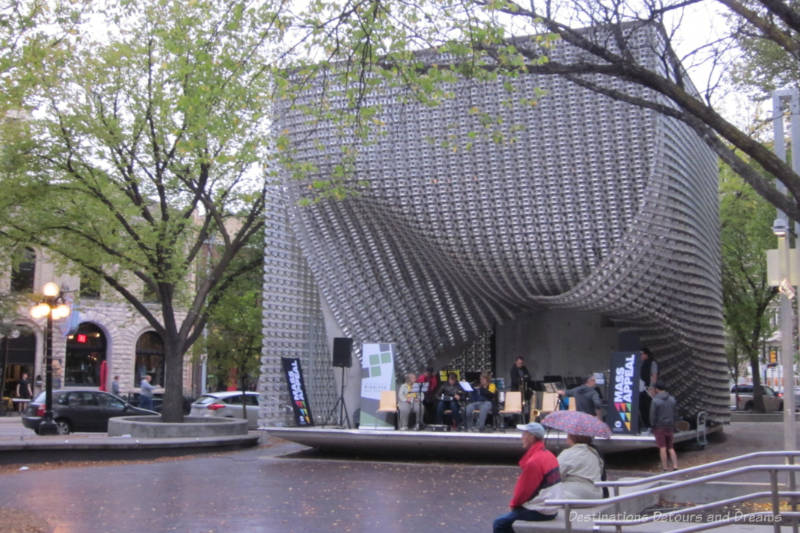 Winnipeg Exchange Cube Outdoor stage with a shell of angled aluminum pieces to create a mesh curtain