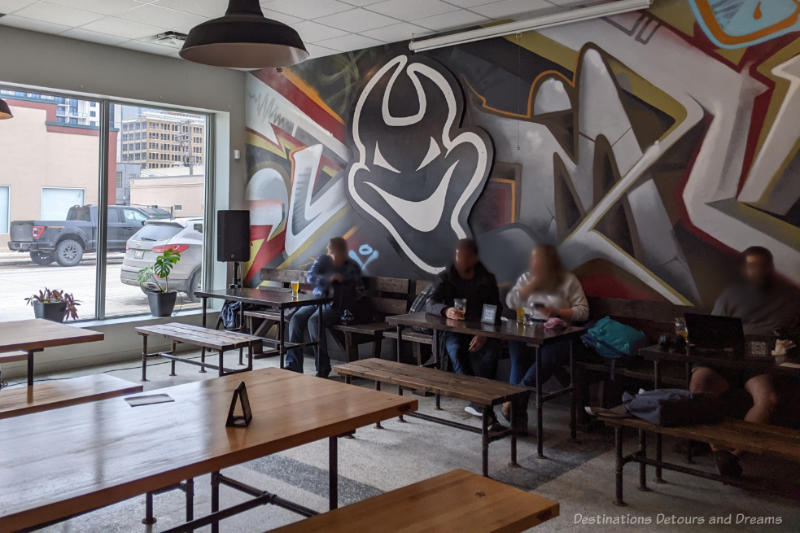 Devil May Care Brewing Long tables in a taproom with a back wall containing a geometric mural