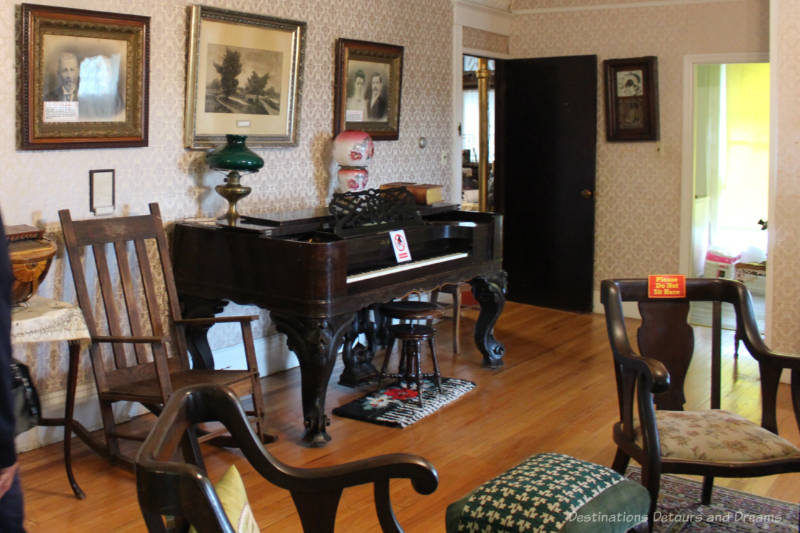 Room in house museum decorated as of early twentieth century features sitting chairs and organ