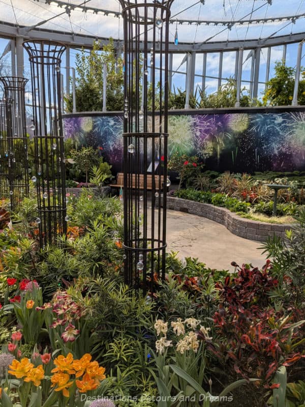 Circular rod pillars inside a bed of blooming spring flowers contain hanging crystals