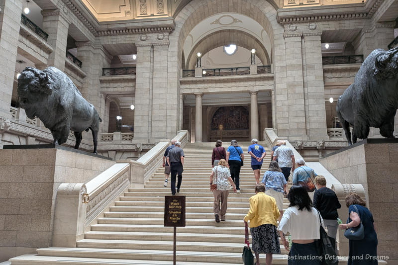 Group of people ascending a grand marble staircase flanked by life-size bronze bison statues