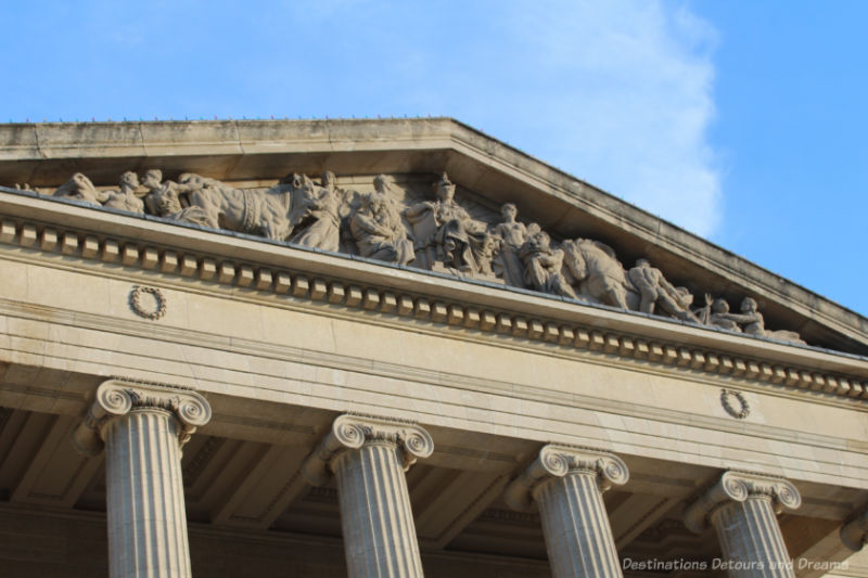 Close-up of a building's triangular pediment containing carved Roman and Greek figures