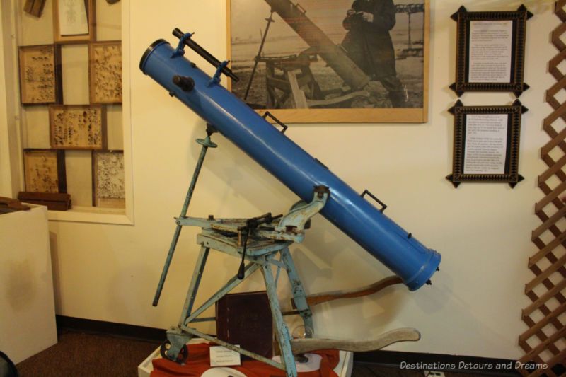 Sipiweske Museum Criddle Telescope Museum exhibit of old blue telescope with photos and mounted insect trays on wall behind it