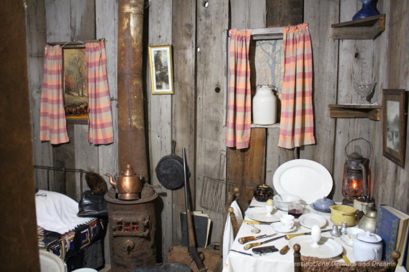 Sipiweske Museum Pioneer Life Room Museum pioneer life exhibit showing kitchen table area beside sleeping cot in room with wood plank walls