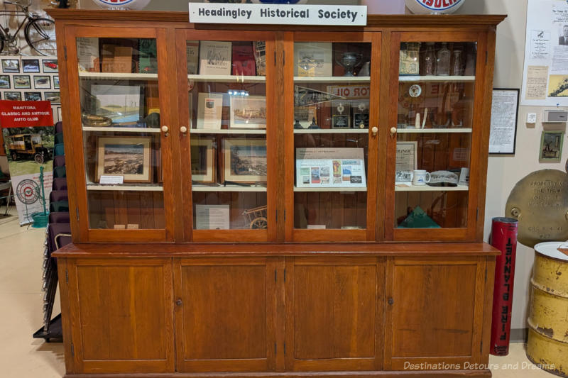 A wooden cabinet with shelves behind glass doors contains a selection of historical documents and memorabilia