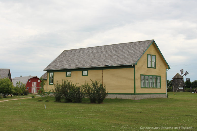 Buildings (yellow wood house with red trim, red barn, and gristmill) in Arborg Heritage Village