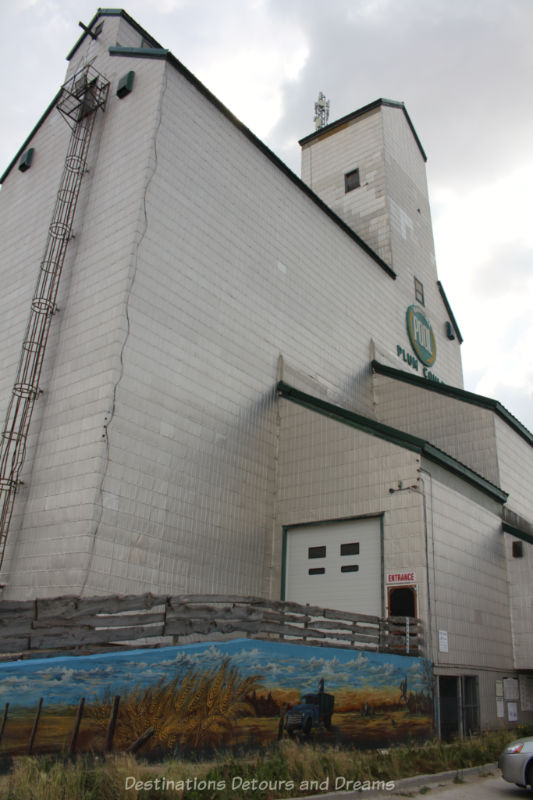 Former white wooden grain elevator now operating as musume and contain a mural of a field of what at its base