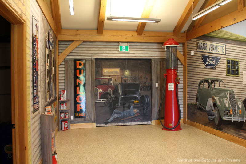 Inside of a wood framed building with murals on two walls showing a vintage garage