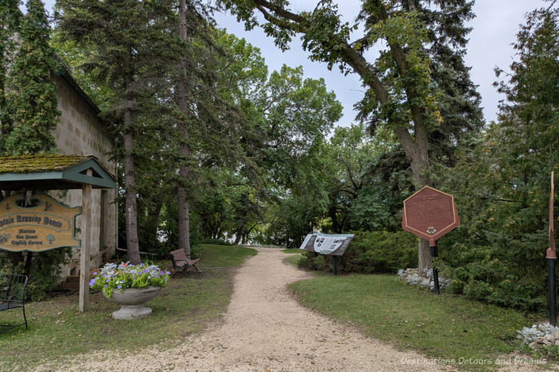 Path through trees at the side of a historic stone house with interpretive signs lining the path
