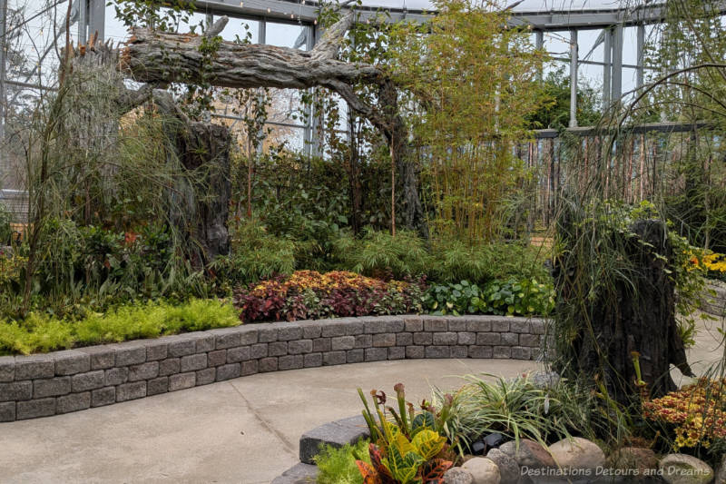 A collection of plants in a brick flower bed with a wooden log archway at back